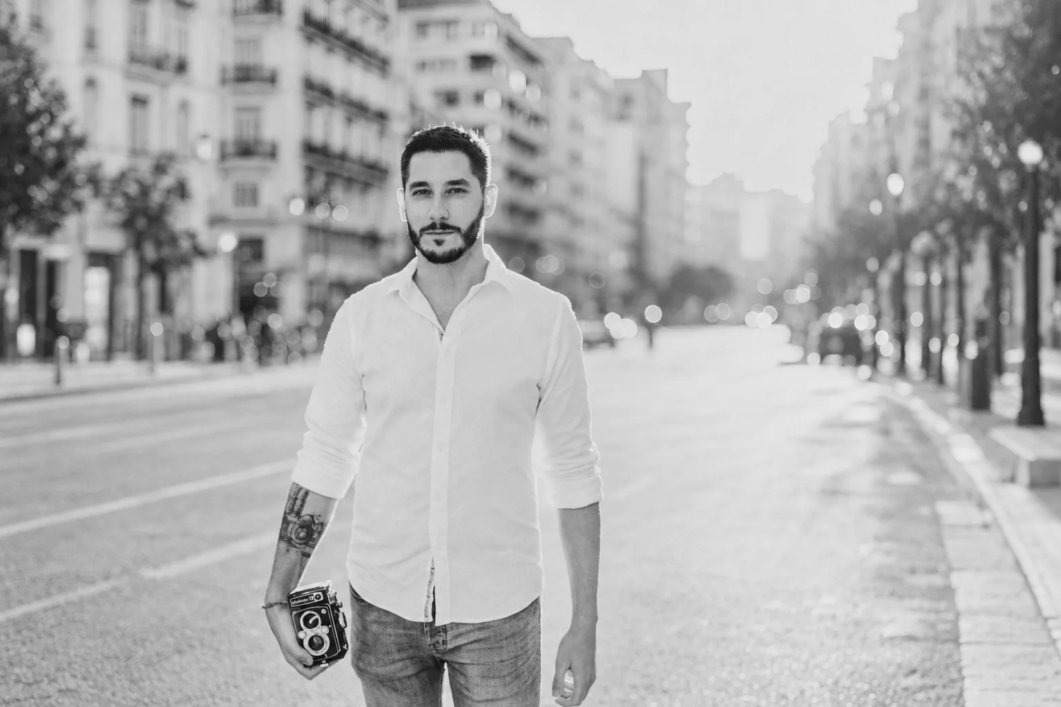 Retrato en blanco y negro de David Bresó con una cámara en una calle urbana.